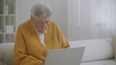 Eine-ältere-Frau,-Die-Auf-Der-Couch-Sitzt,-Druckt-Eine-Nachricht-Auf-Der-Tastatur.-Oma-Benutzt-Einen-Laptop